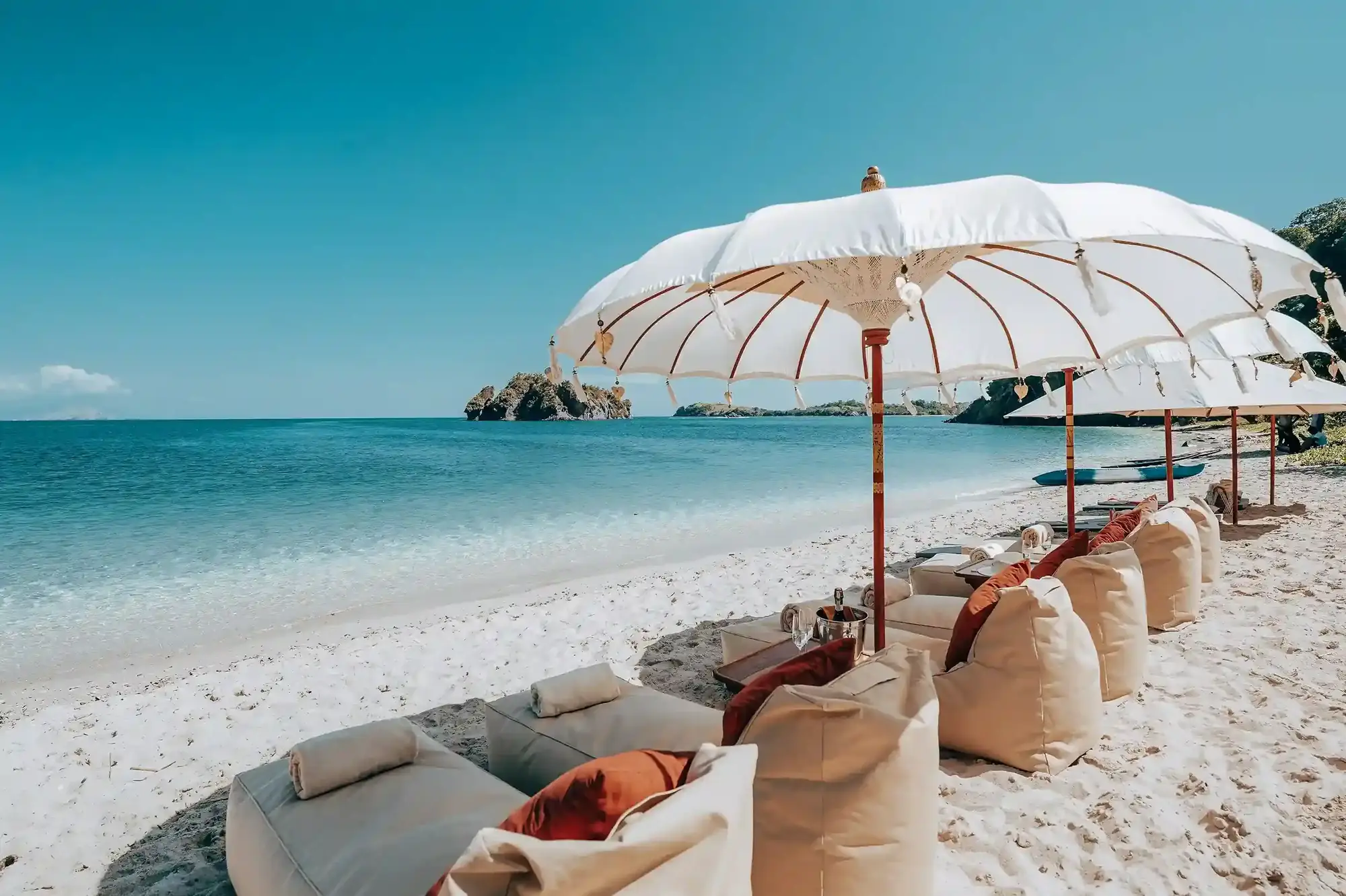 Beach lounge with white parasols and cushions beside a calm sea