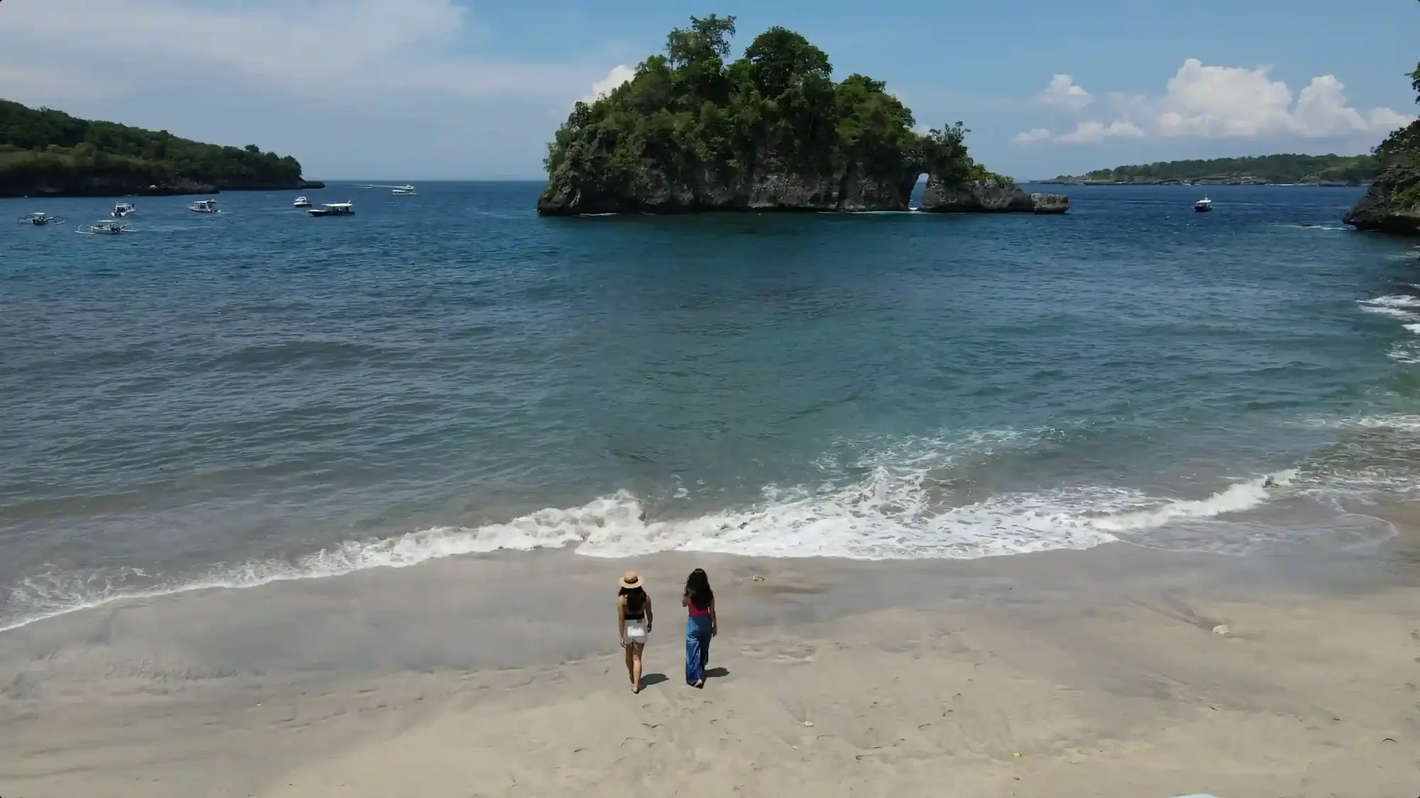Crystal Bay on Nusa Penida with a small rocky islet and two people on the sand