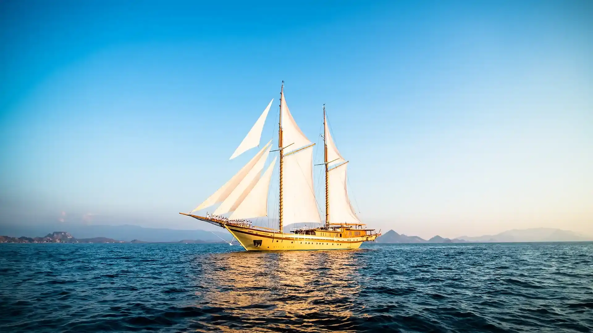 Golden two-masted sailing boat under full sail on open water