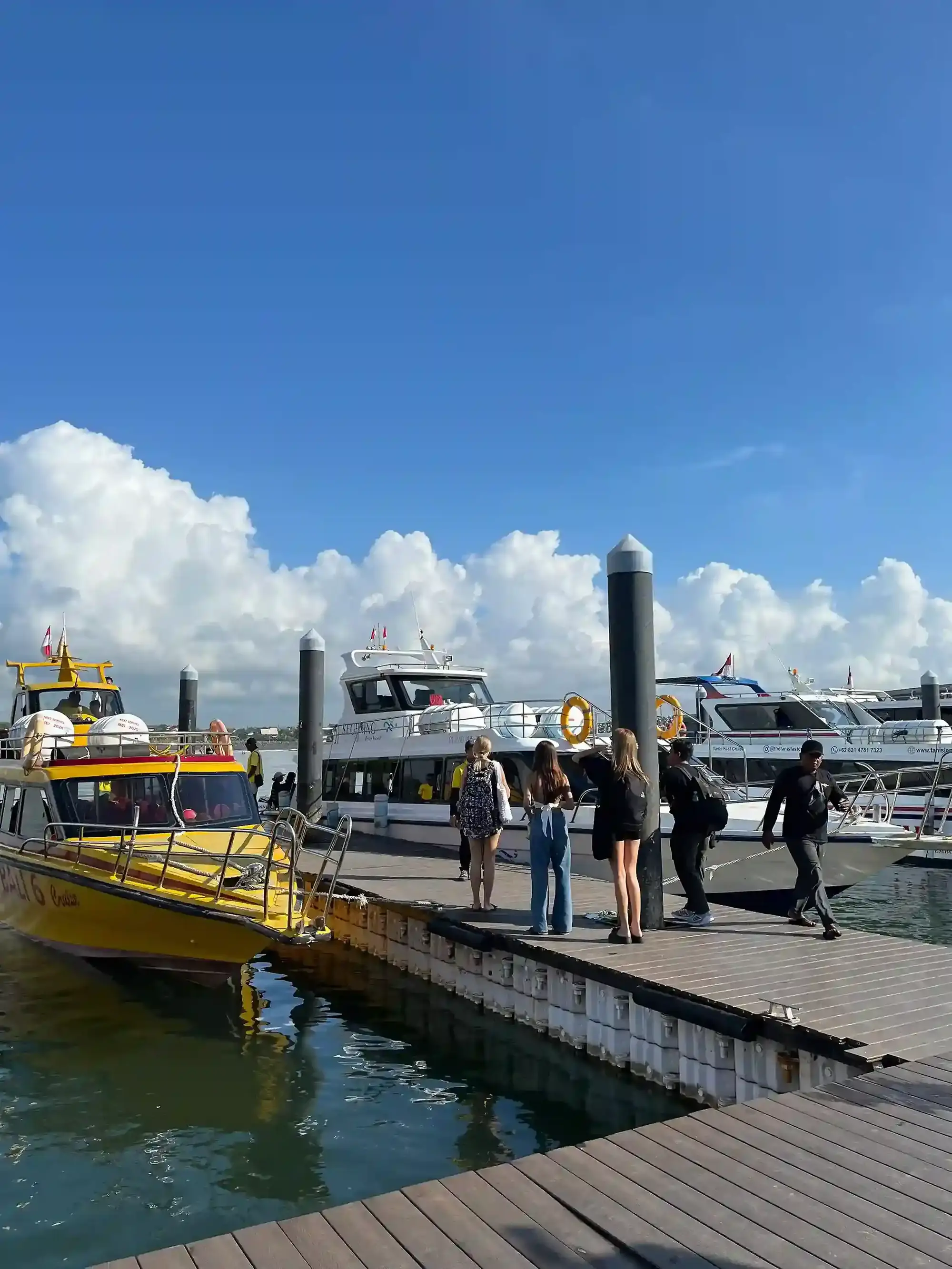 Passengers walking along a pontoon toward fast boats at a Bali harbour